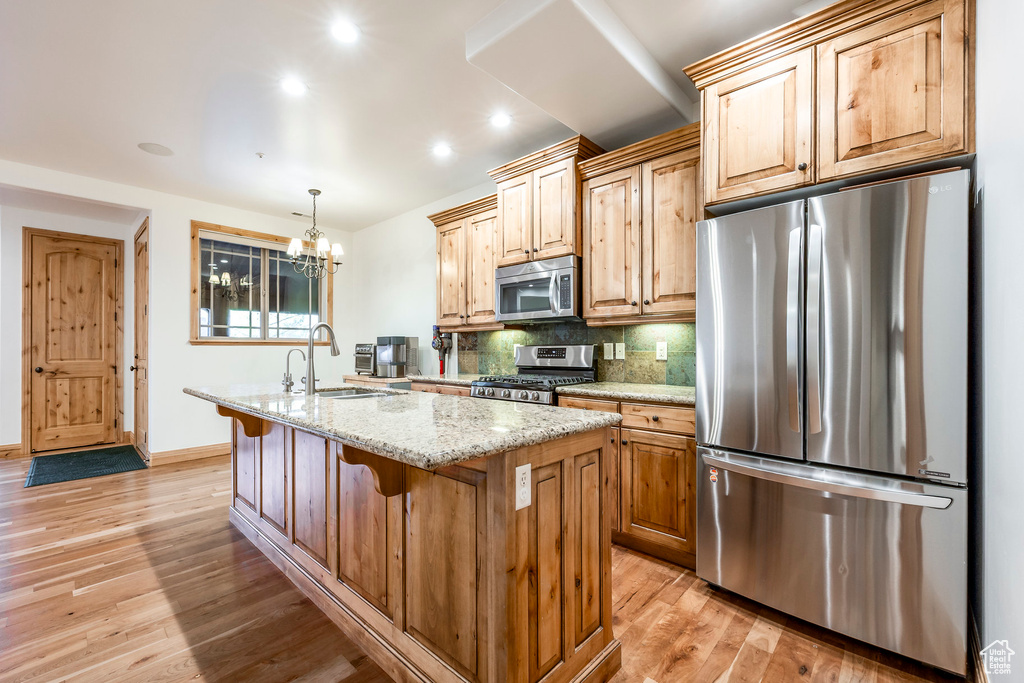 Kitchen featuring stainless steel appliances, light wood-type flooring, an island with sink, tasteful backsplash, and a sink