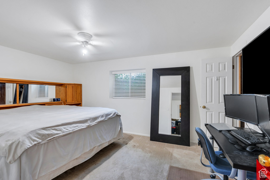 Bedroom with light carpet, a ceiling fan, an office area, and baseboards