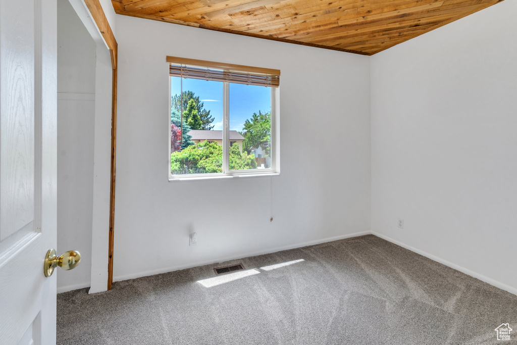 Empty room with wooden ceiling, carpet floors, and baseboards