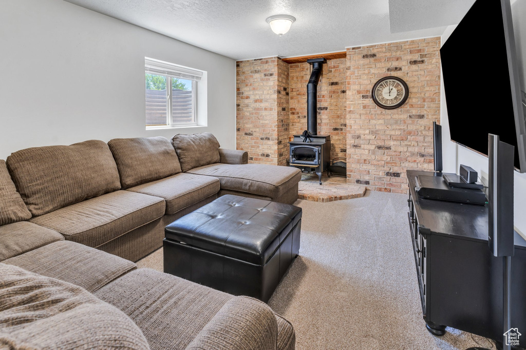 Carpeted living area featuring a wood stove, a textured ceiling, and brick wall
