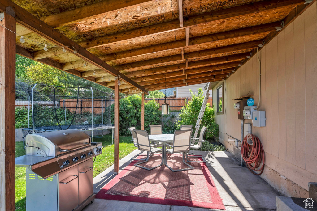 View of patio with a trampoline, outdoor dining area, a fenced backyard, and grilling area
