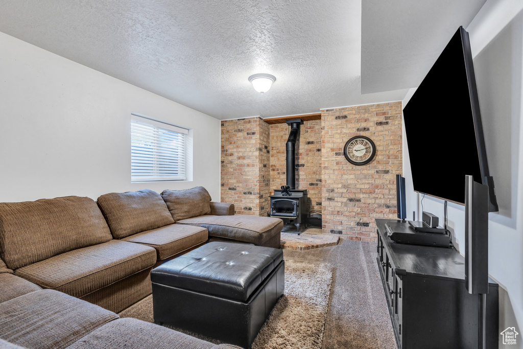 Living room with brick wall, carpet flooring, a wood stove, and a textured ceiling