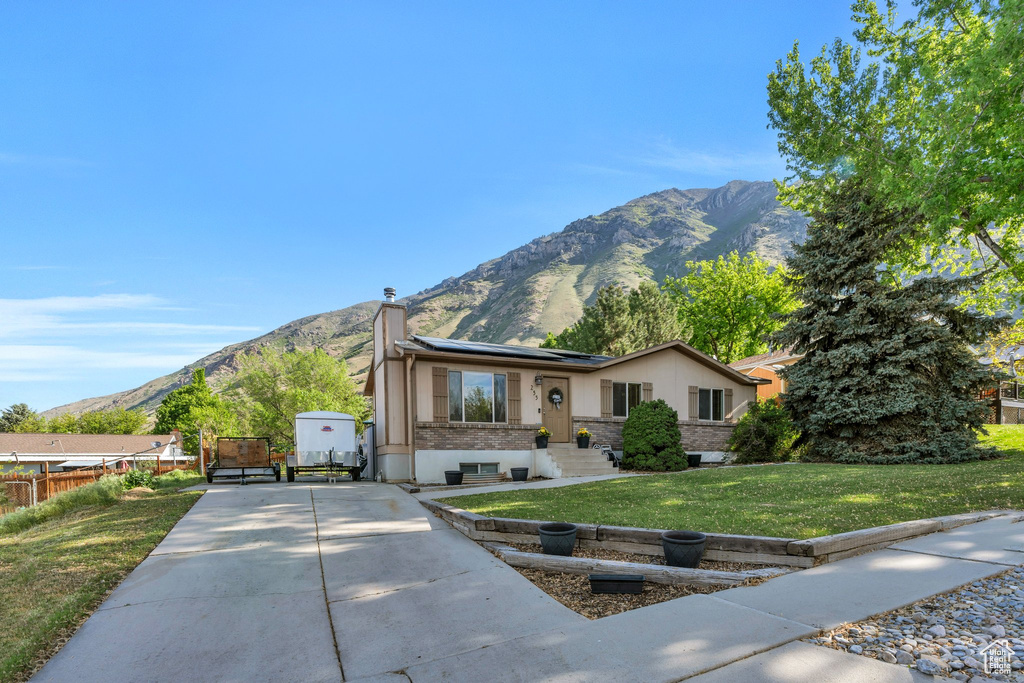 View of front of house with a mountain view, a chimney, roof mounted solar panels, and stucco siding