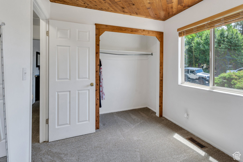 Unfurnished bedroom featuring carpet flooring, wood ceiling, a closet, and baseboards