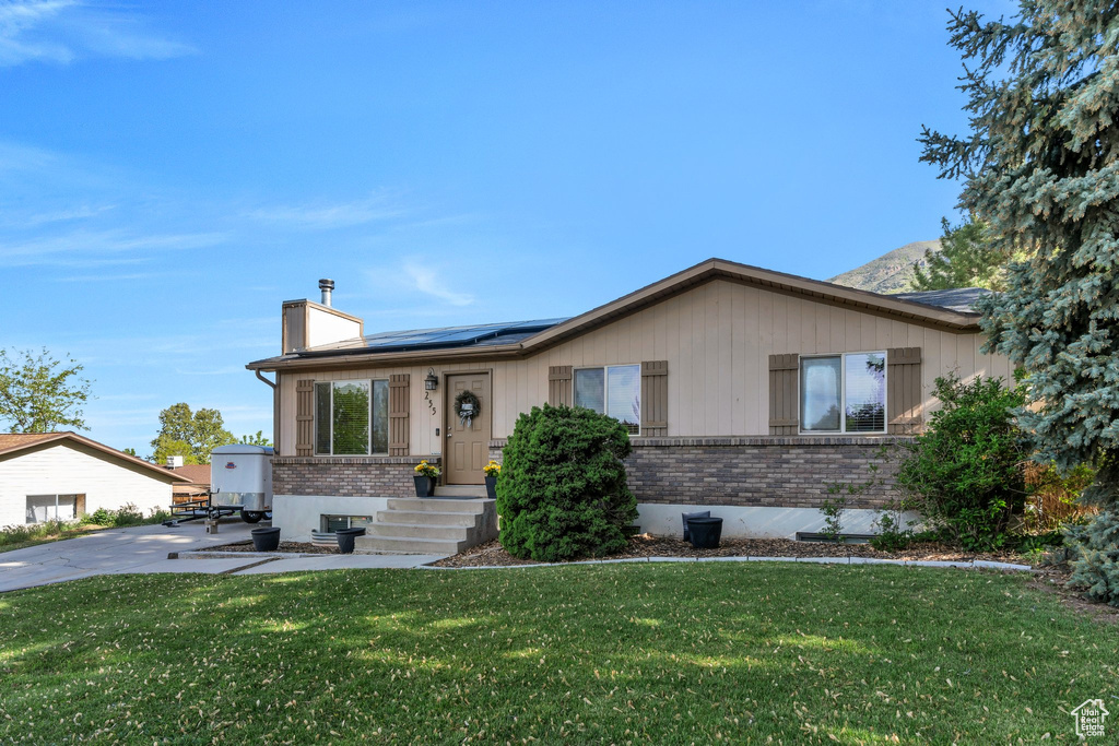 Ranch-style house with brick siding, a chimney, roof mounted solar panels, and a front lawn