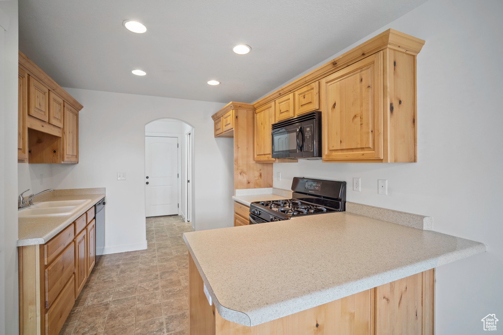 Kitchen featuring black appliances, a sink, a peninsula, arched walkways, and light countertops