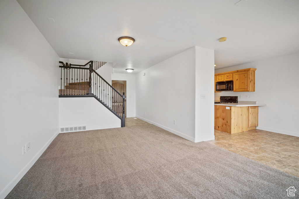 Unfurnished living room featuring stairway, light colored carpet, and baseboards