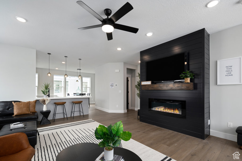 Living room with wood finished floors, baseboards, ceiling fan, a fireplace, and recessed lighting
