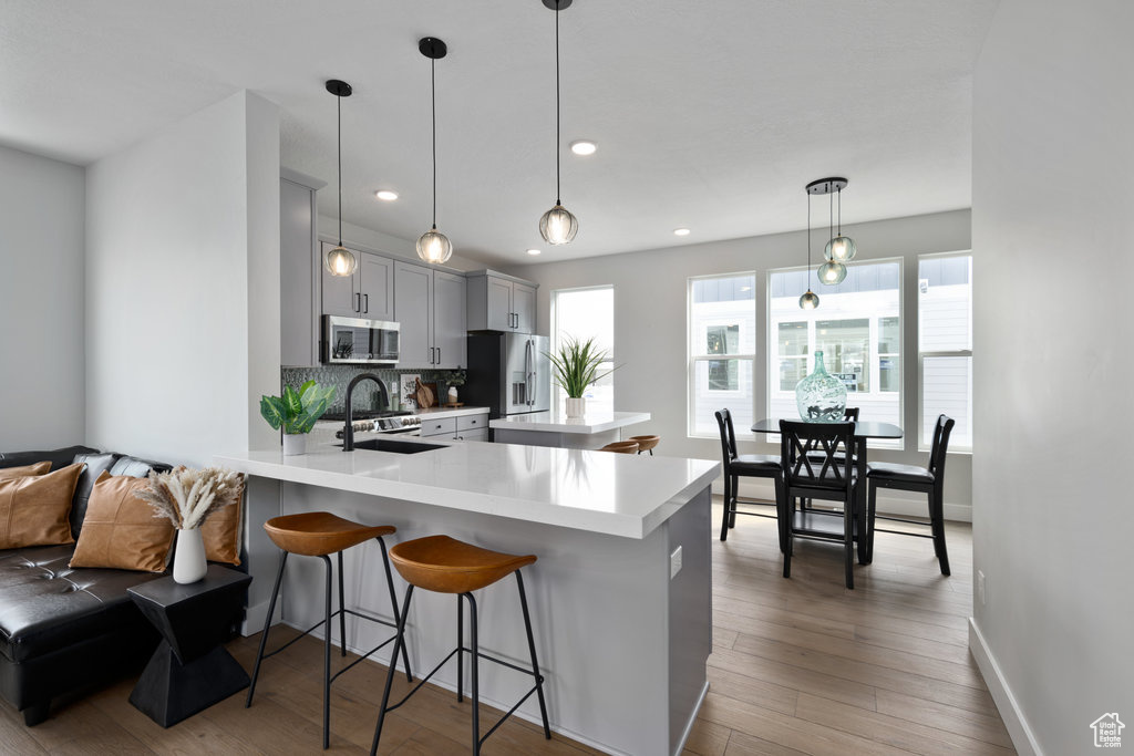 Kitchen featuring appliances with stainless steel finishes, a sink, light countertops, a peninsula, and a breakfast bar