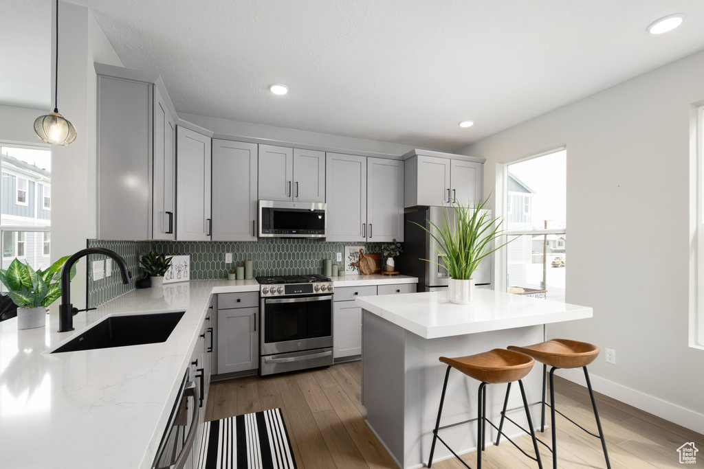 Kitchen featuring appliances with stainless steel finishes, a sink, backsplash, gray cabinets, and a breakfast bar