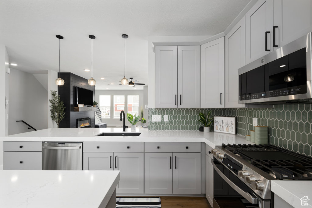 Kitchen with stainless steel appliances, a sink, a peninsula, light countertops, and decorative backsplash