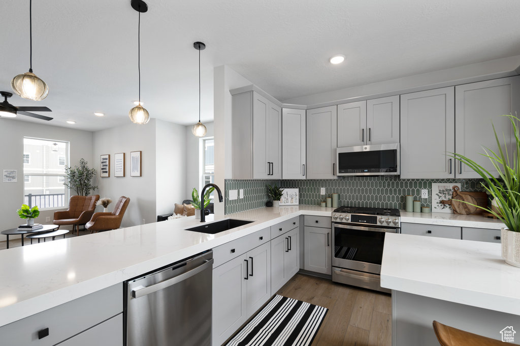 Kitchen featuring stainless steel appliances, a sink, light countertops, backsplash, and pendant lighting