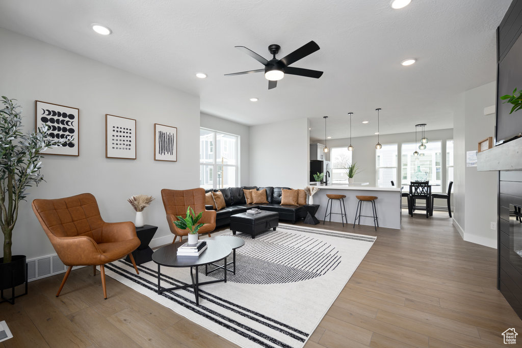 Living room featuring light wood-type flooring, ceiling fan, baseboards, recessed lighting, and a tiled fireplace