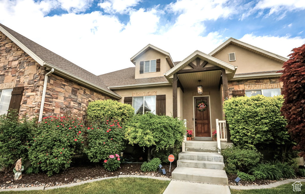 View of front of home with stucco siding, stone siding, and a shingled roof
