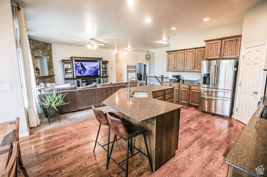 Kitchen featuring stainless steel fridge with ice dispenser, a sink, a ceiling fan, wood finished floors, and a breakfast bar area