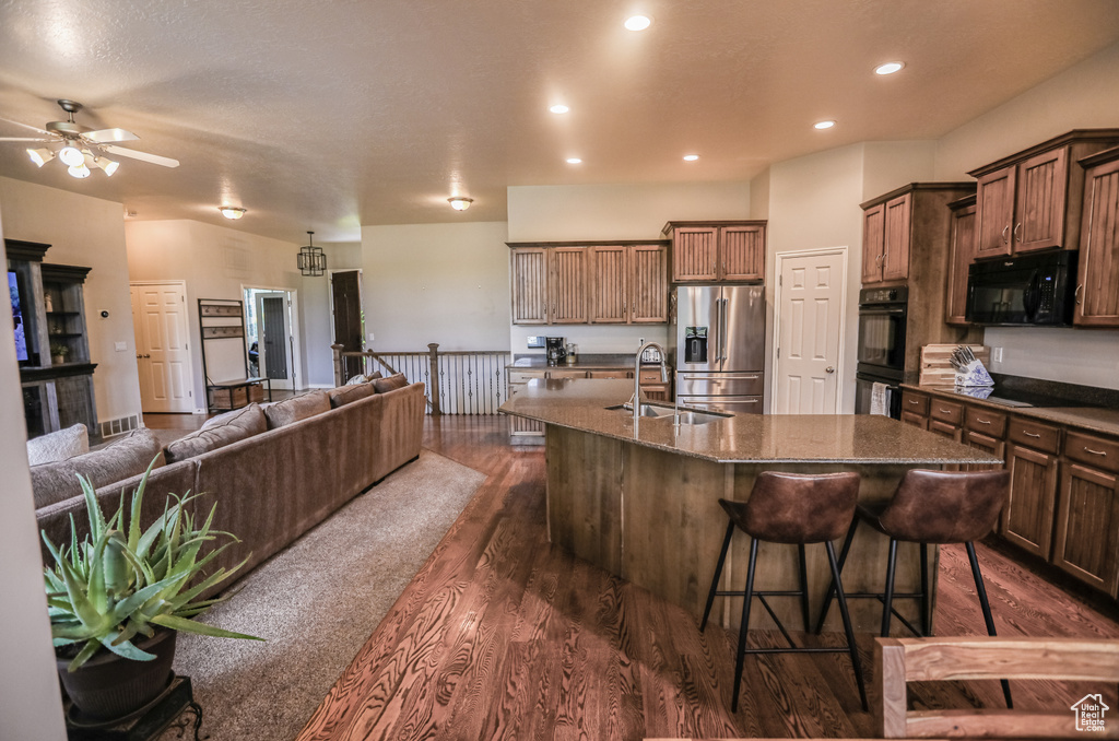 Kitchen with black appliances, a sink, a center island with sink, dark wood-style flooring, and open floor plan
