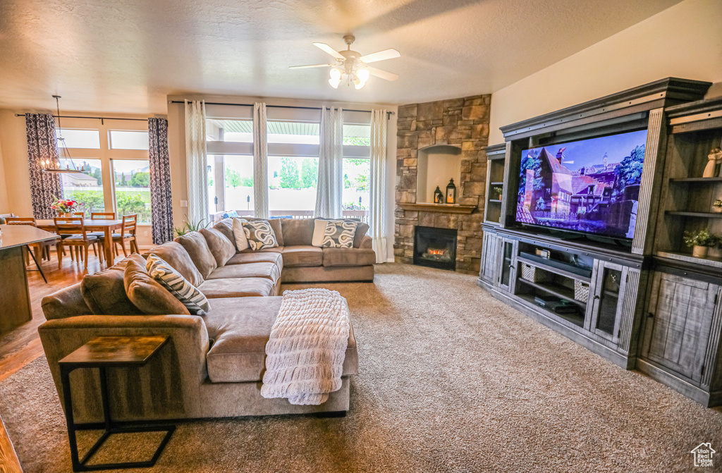 Carpeted living room featuring ceiling fan, a fireplace, and a chandelier