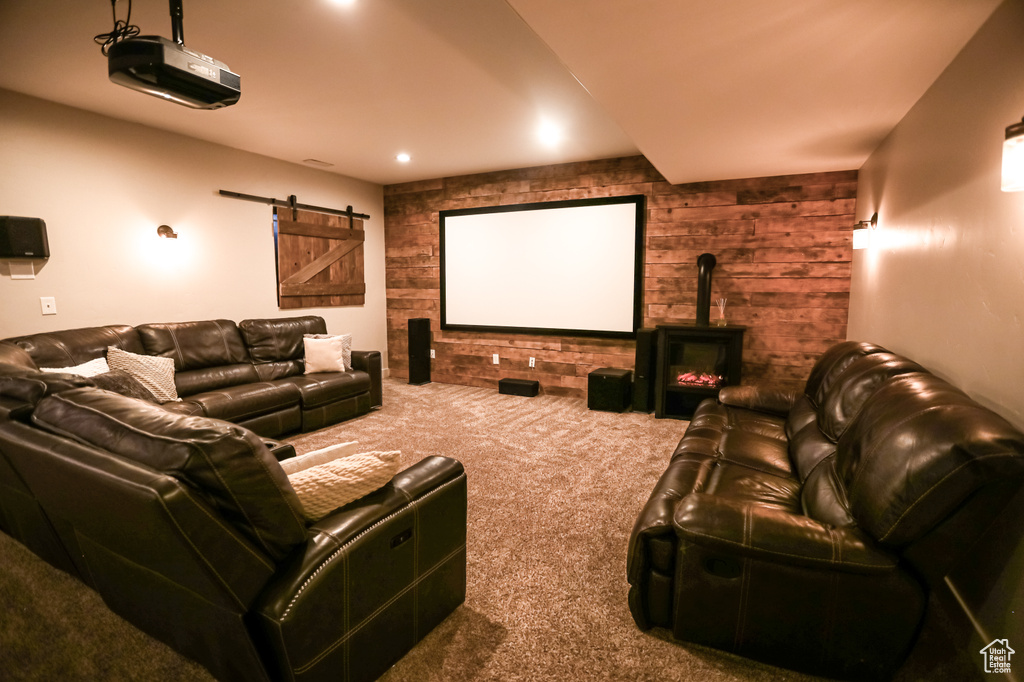 Carpeted home theater room with a barn door, wood walls, and a wood stove