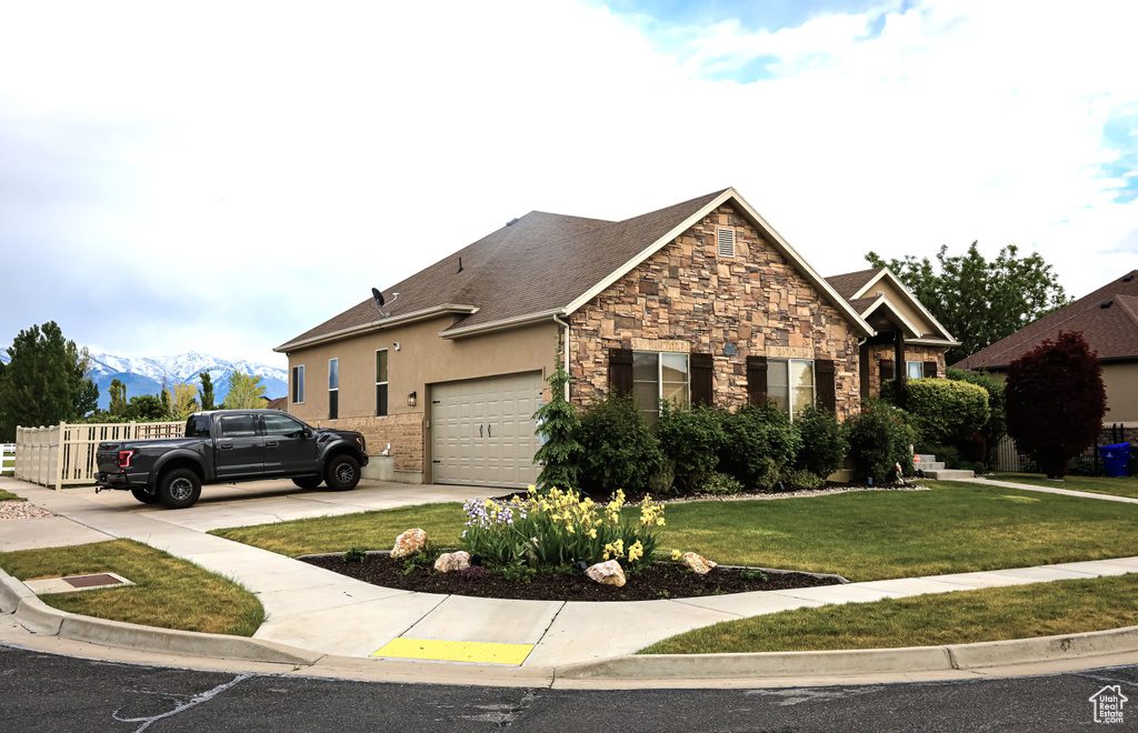View of front of home with stone siding, a garage, a front yard, concrete driveway, and a mountain view