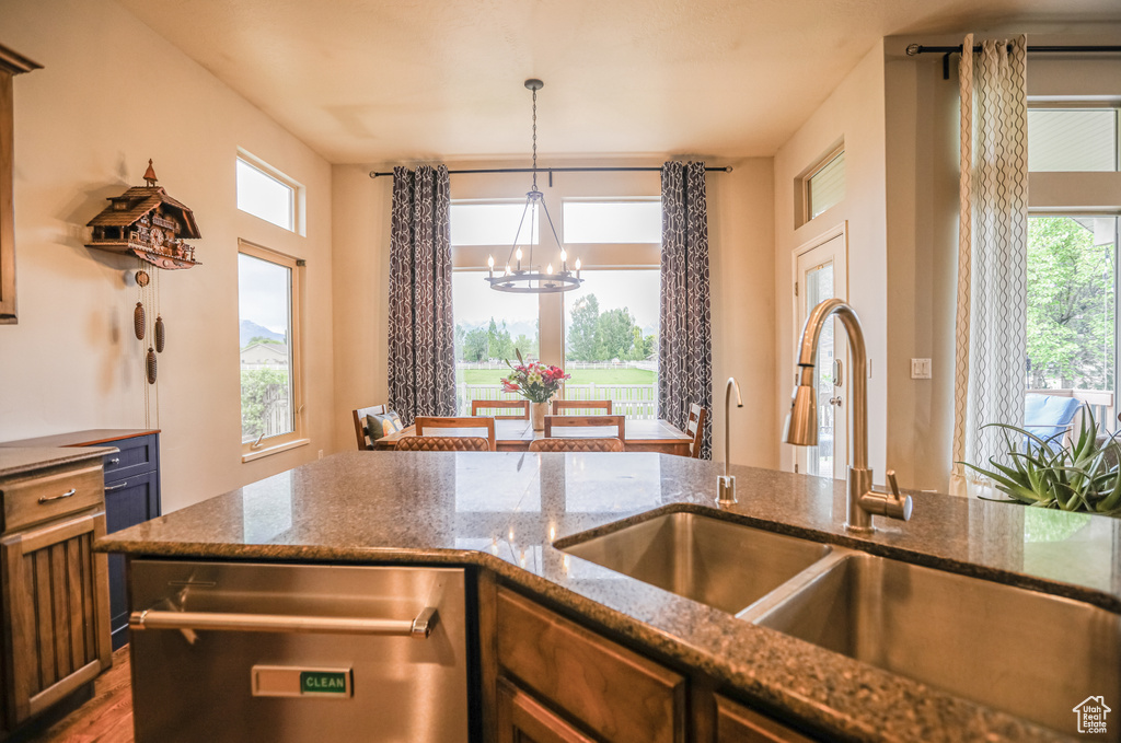 Kitchen featuring stainless steel dishwasher, a chandelier, a sink, decorative light fixtures, and dark stone counters