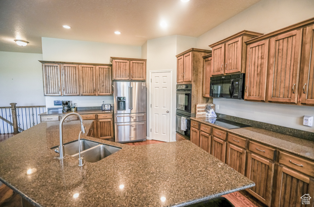 Kitchen featuring black appliances, a sink, a large island with sink, brown cabinetry, and dark wood-style flooring