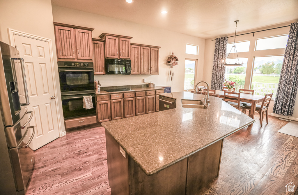 Kitchen featuring a sink, black appliances, a large island with sink, wood finished floors, and recessed lighting