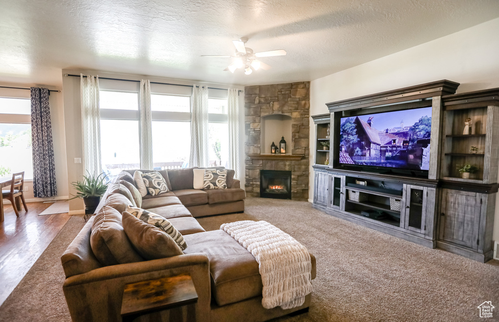 Living area with ceiling fan, a stone fireplace, and a textured ceiling