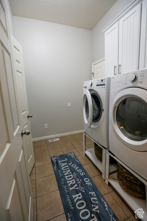 Clothes washing area with washing machine and clothes dryer, cabinet space, tile patterned floors, and baseboards