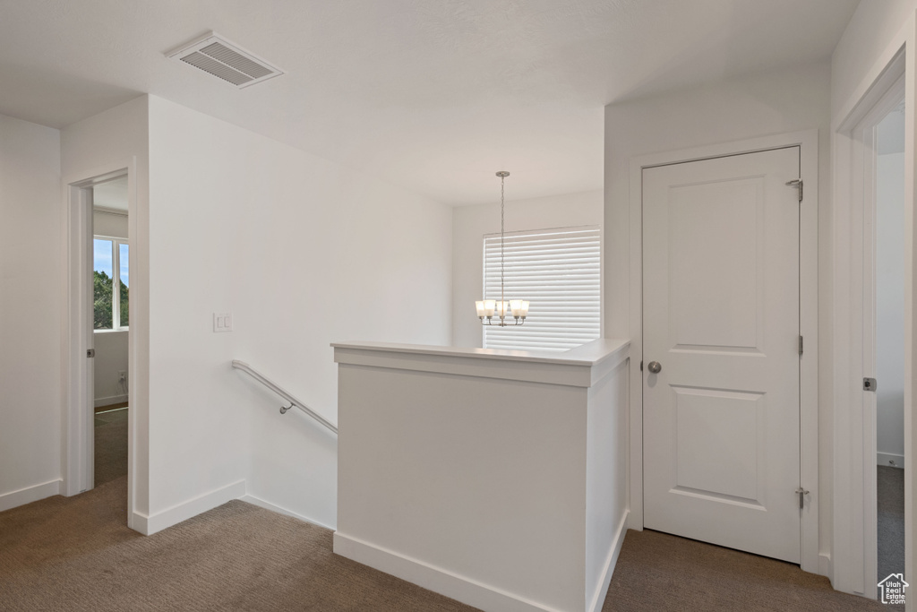 Hall with an upstairs landing, healthy amount of natural light, carpet flooring, and a chandelier