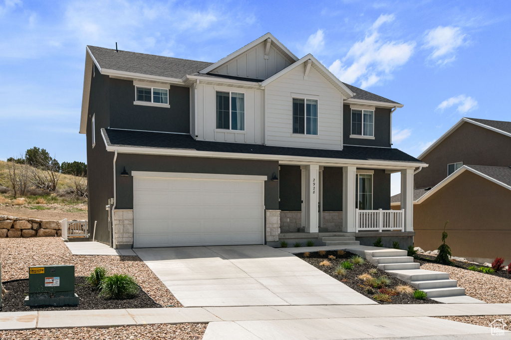 View of front of property featuring board and batten siding, a porch, stone siding, an attached garage, and driveway