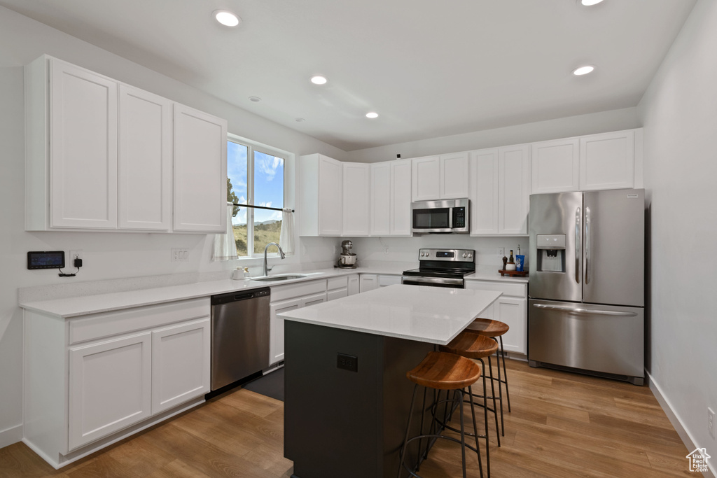 Kitchen featuring appliances with stainless steel finishes, a sink, a breakfast bar, white cabinetry, and recessed lighting