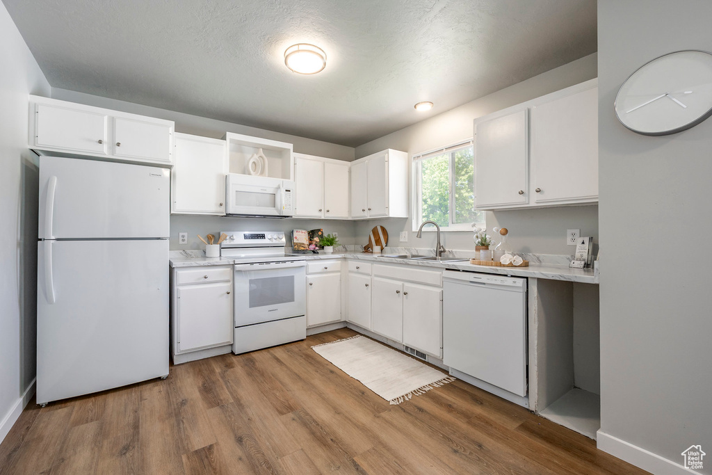 Kitchen featuring white appliances, a sink, wood finished floors, and white cabinets