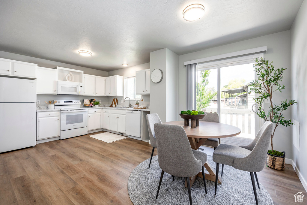 Kitchen with white appliances, light countertops, light wood-style flooring, white cabinetry, and a sink