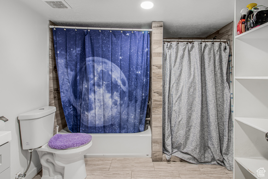 Full bathroom featuring toilet, shower / tub combo, and a textured ceiling