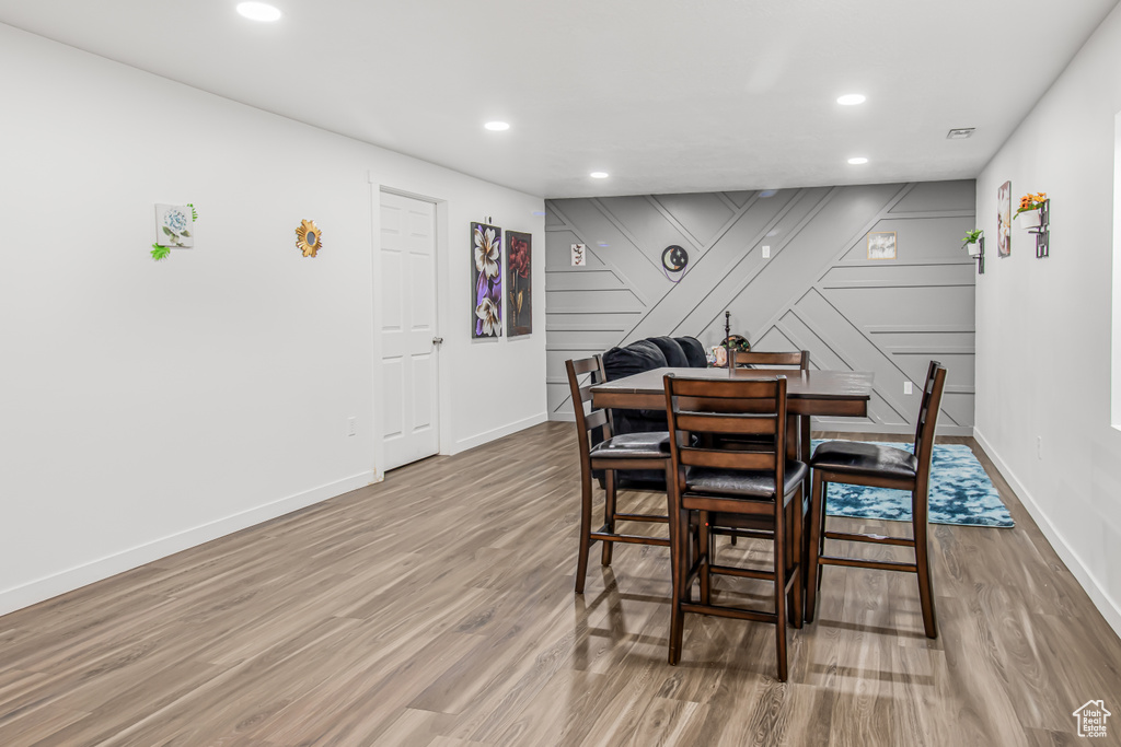 Dining room with wood finished floors, baseboards, recessed lighting, and a decorative wall