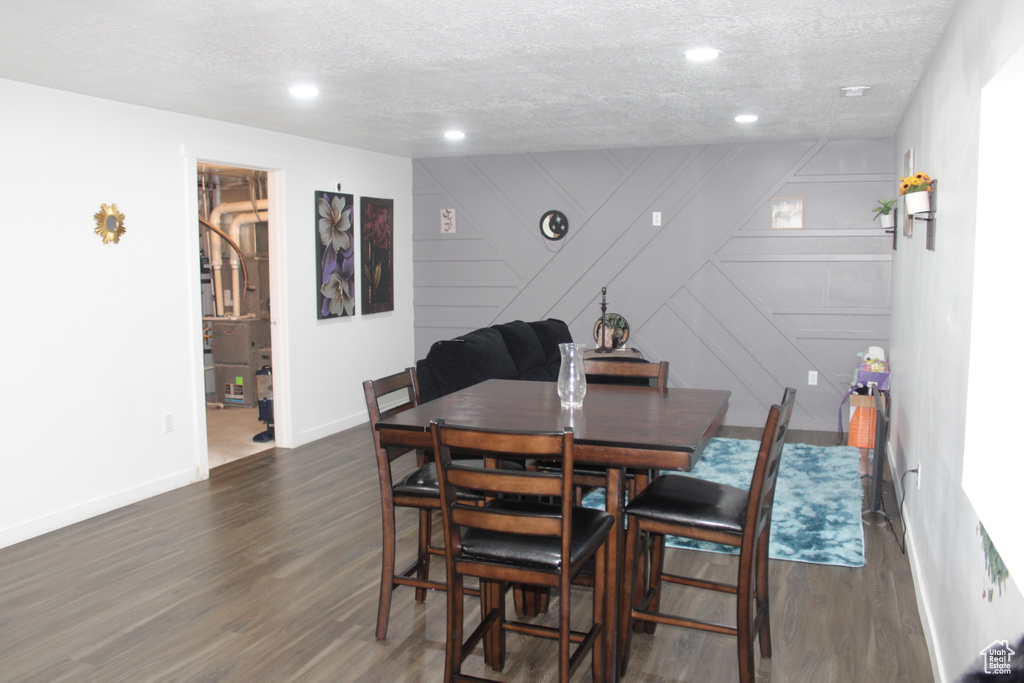 Dining space featuring dark wood-type flooring, a textured ceiling, baseboards, recessed lighting, and a decorative wall