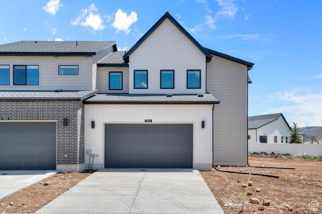 View of front of house featuring a garage, driveway, fence, brick siding, and a shingled roof