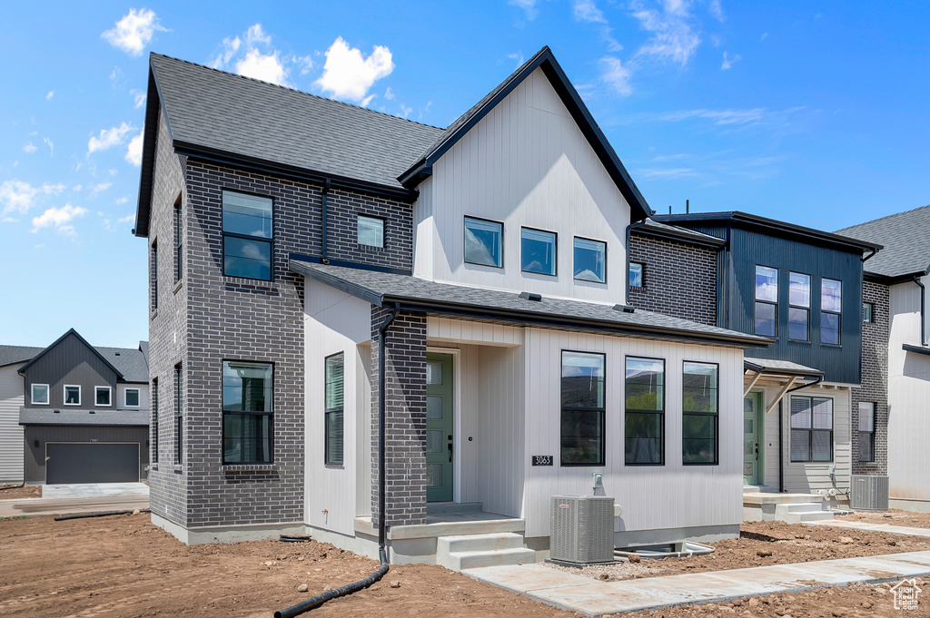 View of front of home with central AC, brick siding, a garage, and roof with shingles