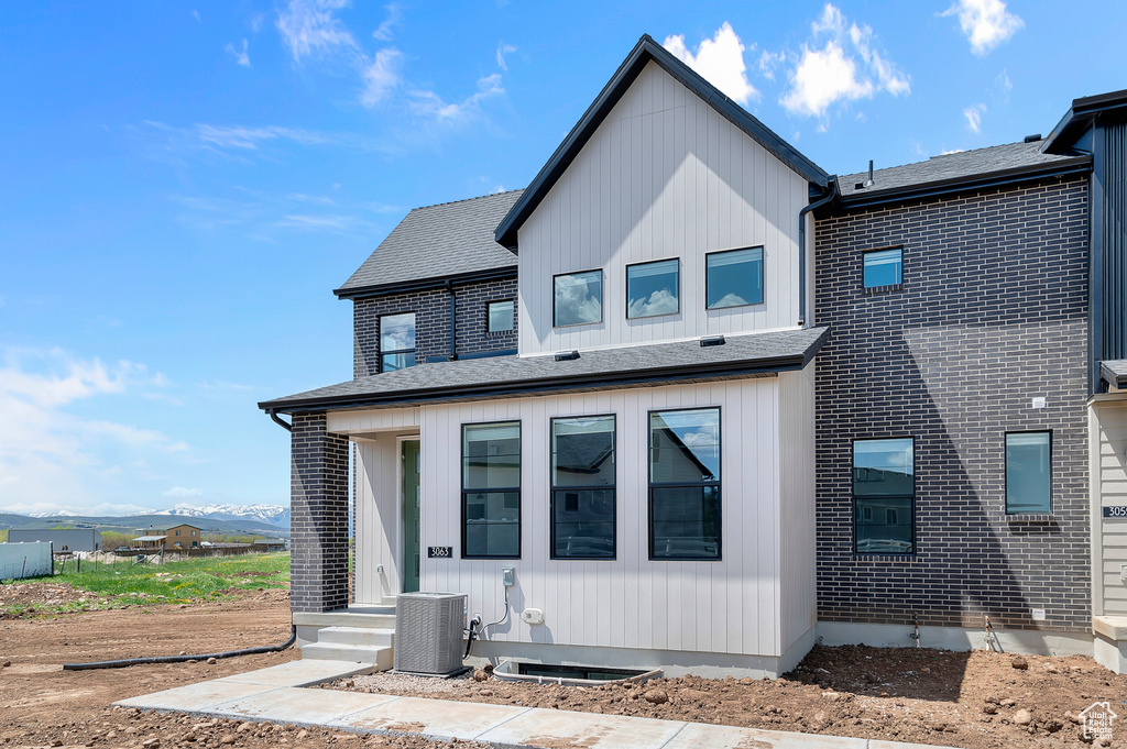 Rear view of property with roof with shingles, cooling unit, and a mountain view