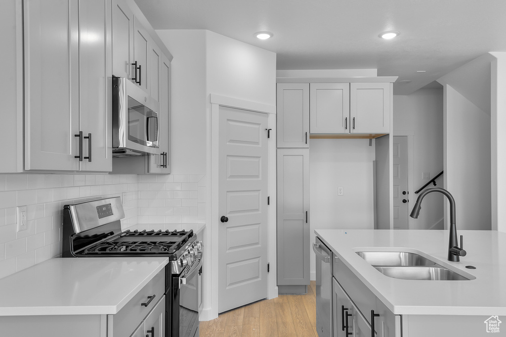 Kitchen with stainless steel appliances, a sink, light countertops, light wood-type flooring, and recessed lighting