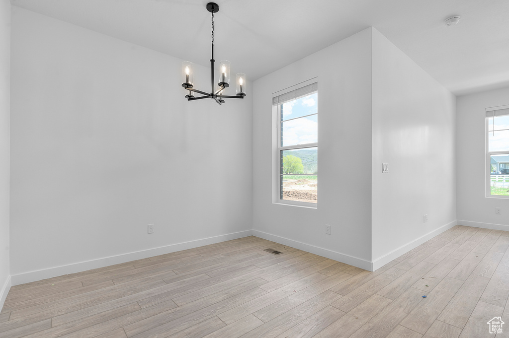 Unfurnished dining area with a chandelier, light wood finished floors, plenty of natural light, and baseboards