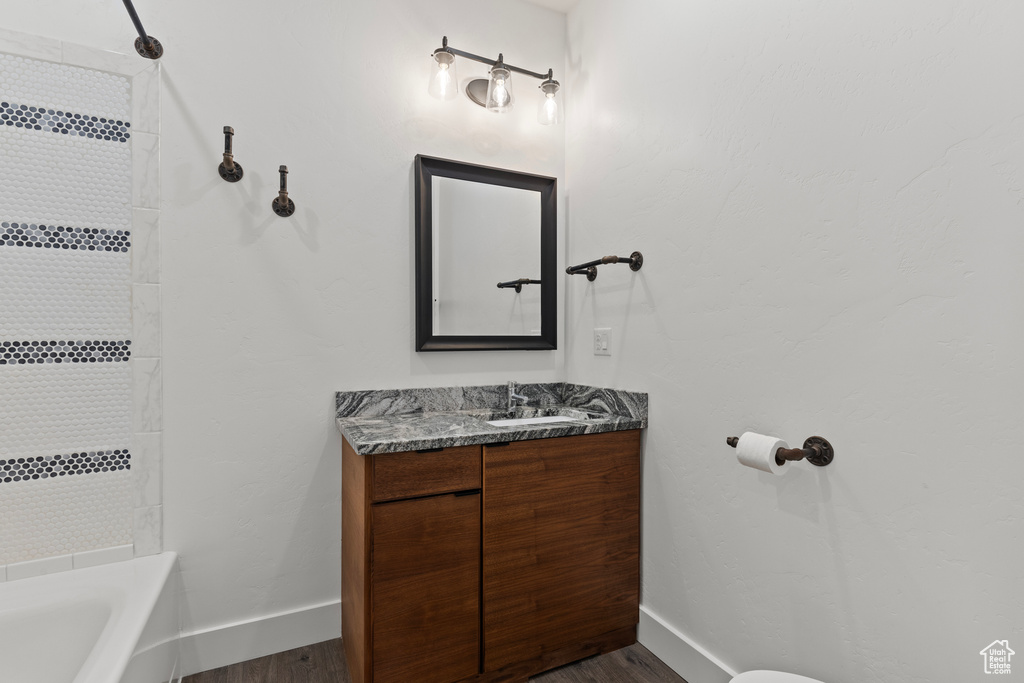 Full bathroom featuring baseboards, wood finished floors, vanity, and bathtub / shower combination