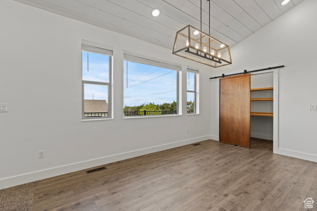 Unfurnished bedroom with baseboards, wood finished floors, a barn door, a spacious closet, and recessed lighting