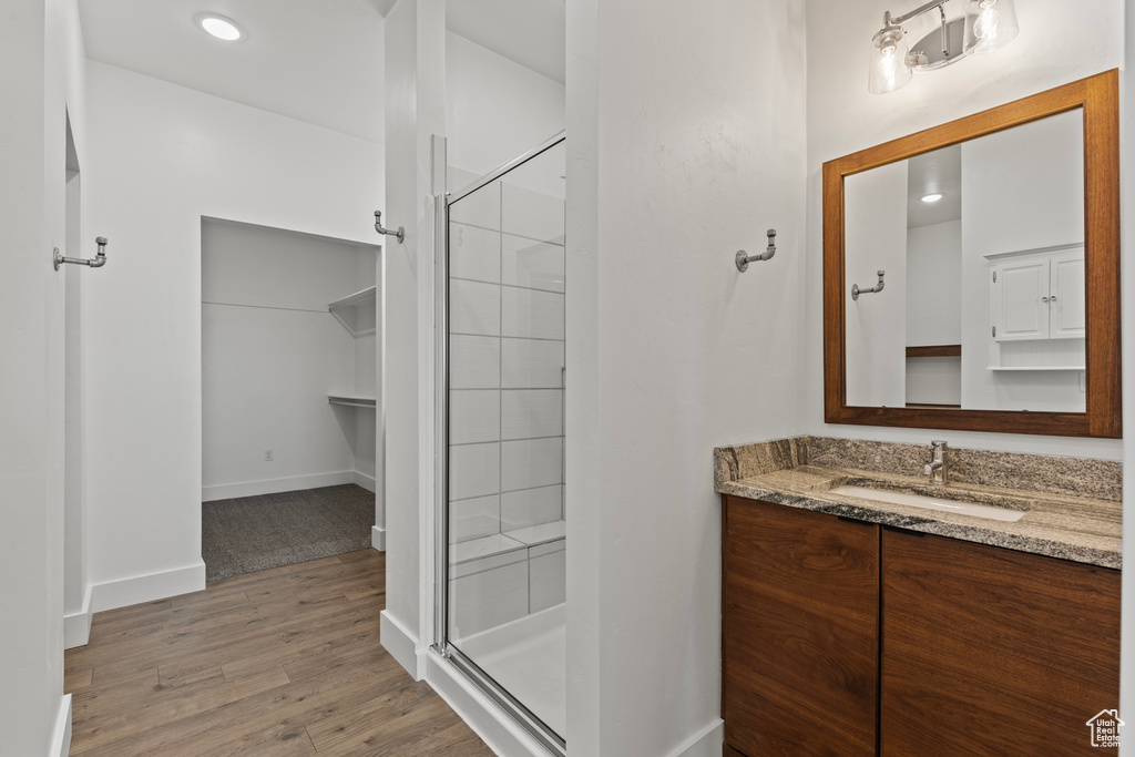 Bathroom featuring a stall shower, wood finished floors, vanity, baseboards, and recessed lighting