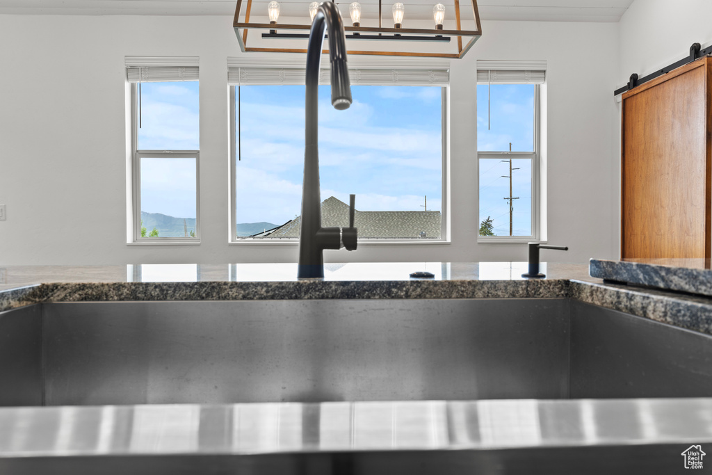 Kitchen view of dark stone countertops, a barn door, a sink, and hanging light fixtures