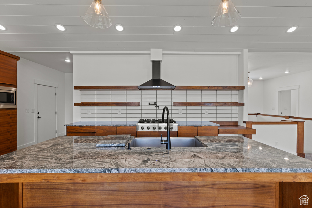 Kitchen with open shelves, brown cabinets, wall chimney range hood, stainless steel microwave, and recessed lighting