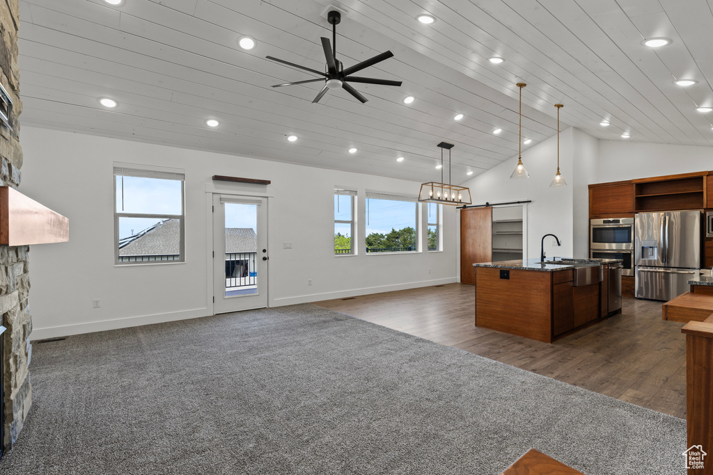Kitchen featuring appliances with stainless steel finishes, a barn door, a kitchen island with sink, open shelves, and open floor plan