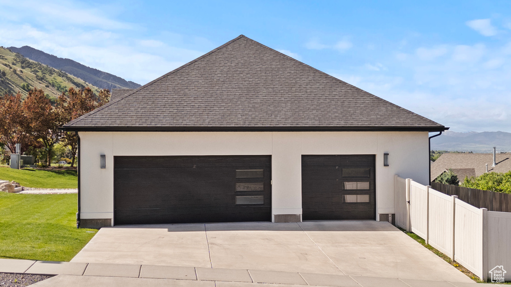 View of side of home featuring a mountain view, roof with shingles, a garage, and stucco siding
