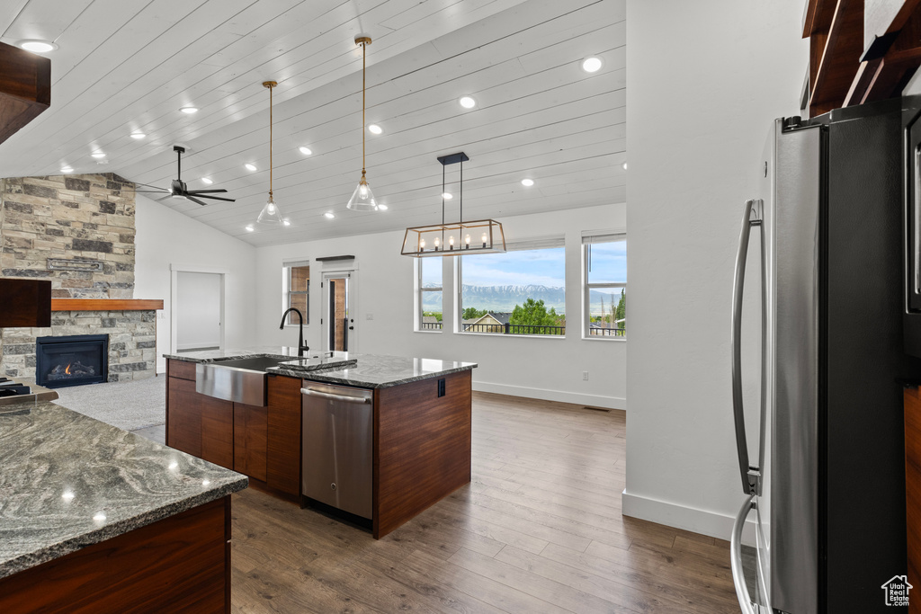 Kitchen with appliances with stainless steel finishes, a sink, a stone fireplace, a ceiling fan, and dark wood-type flooring