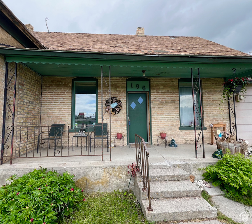 Doorway to property featuring covered porch, brick siding, a chimney, and roof with shingles